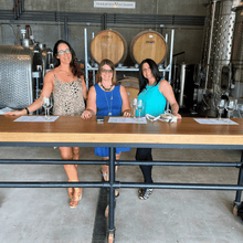 Load image into Gallery viewer, Three ladies dressed up in their best summer apparel pose for a picture, standing in the cellar and tasting room of Terravista vineyards on the Naramata Bench in Penticton, BC.  | Farm to Glass Wine Tours
