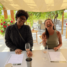 Load image into Gallery viewer, Two women enjoying a joyful moment, laughing hysterically at the tasting room bar of Bartier Bros Winery in Oliver, BC. The vibrant atmosphere adds to the fun as they savour delicious wines | Farm to Glass Wine Tours
