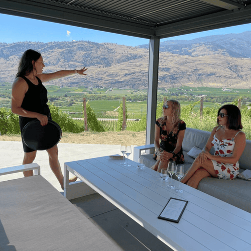 Two women enjoying a wine tasting at Phantom Creek Estates with an ambassador. They learn about the Black Sage Bench terroir, savoring exquisite wines amidst stunning vineyard views.  | Farm to Glass Wine Tours