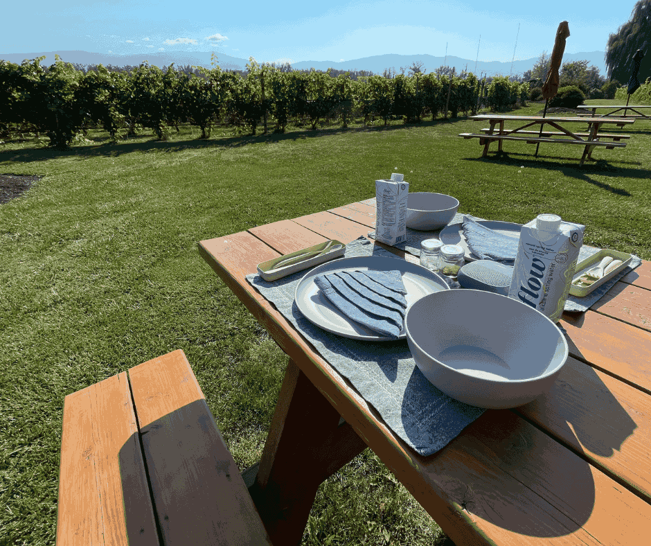 a picnic bench is set up for an eco-friendly lunch with linens and sustainably packaged water, overlooking a vineyard in East Kelowna, BC | Farm to Glass Wine Tours