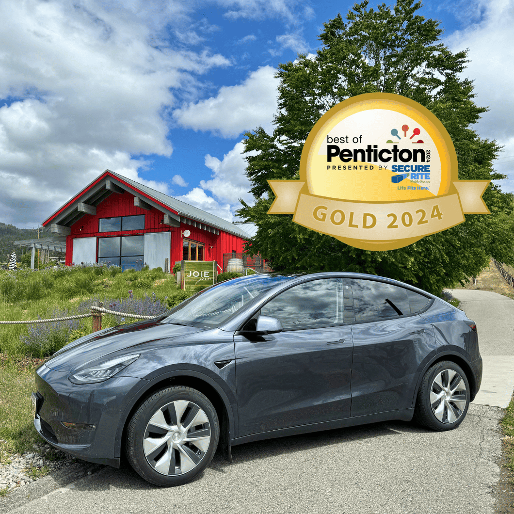 Picture of a Tesla Model Y in front of JoieFarm winery in Naramata BC with a logo that states that Farm to Glass Wine Tours won Gold for Best of Penticton - Best Wine Tour