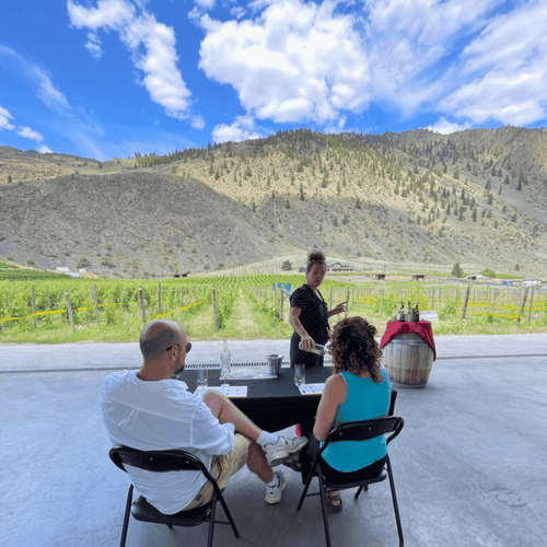 Two guests experiencing a private tasting at Clos du Soleil winery in the Similkameen Valley. The picturesque backdrop of mountains and vineyards adds to the charm as they savor exquisite wines.  Farm to Glass Wine Tours